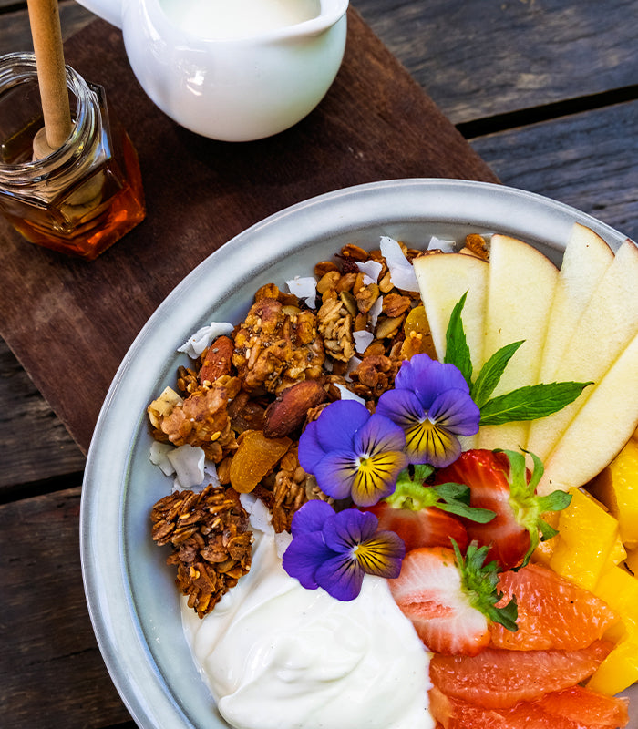 Granola bowl with yoghurt, fruits, and edible flowers on a wooden surface.